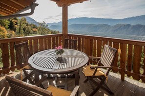 A wooden deck with a round table and chairs, a potted plant, and a view of distant mountains. - Apartment 'Pföslhof Weinberg' with Mountain View, Shared Garden and Wi-Fi (Leifers)