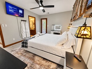 Ein Hotelzimmer mit einem Bett, einem an der Wand befestigten Fernseher, einem Deckenventilator, einem Schreibtisch mit einer Lampe und einem Spiegel.