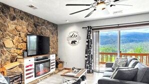 Een woonkamer met een stenen muur, een open haard, een televisie en een balkon met uitzicht.