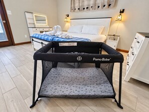 Una culla per bambini PamoBabe in una camera d'albergo con un letto, comodini e lampade a parete.
