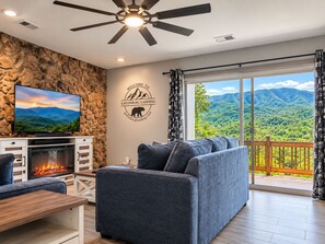 Un salon moderne avec une cheminée, un téléviseur et une grande fenêtre donnant sur les montagnes.