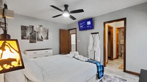 Een slaapkamer met een bed, een plafondventilator, een televisie en een badkamer zichtbaar door een geopende deur.