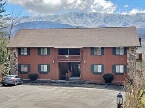 Un bâtiment à deux étages, doté d’une façade en pierre, d’un balcon en bois et offrant une vue sur des montagnes enneigées.
