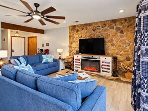 Una sala de estar con pared de piedra, chimenea, televisor y ventilador de techo.