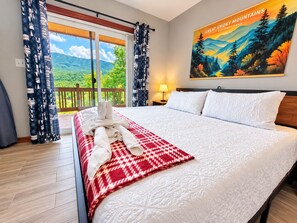 Une chambre d’hôtel avec un grand lit, une vue sur les montagnes par la fenêtre et un tableau représentant les Great Smoky Mountains.