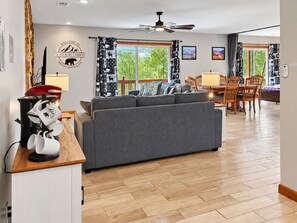 Un salon moderne avec un canapé gris, une table à manger en bois et des chaises. On y trouve également un ventilateur de plafond, une machine à café et un panneau d’accueil indiquant « Bienvenue à Smithsburg Landing ».