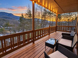 Una terraza de madera con mobiliario exterior, con vista a un paisaje montañoso.