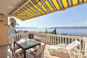 A balcony with a table and chairs, a satellite dish, and a view of the sea and mountains. - Holiday apartment with terrace and barbecue (Novi Vinodolski)