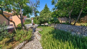 Ein Kiesweg führt durch einen Garten mit einer Steinmauer und verschiedenen Pflanzen.