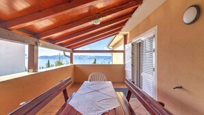 Ein Balkon mit Holztisch und Bank, Blick auf das Meer und ein Berg im Hintergrund.