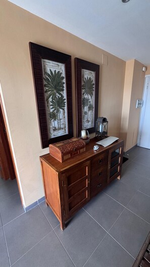 A wooden cabinet with drawers and a small table, a framed picture of palm trees on the wall, and a door in the background. - Avenida Papa Luna, 139, Peñíscola Stilmar, less than 1 minute from the beach!!!!!" (Peñíscola)