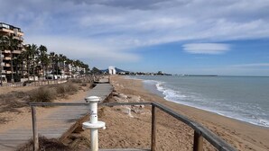 Un muelle de madera que conduce a una playa, con vista despejada al océano y una montaña distante.