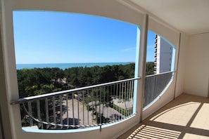 Ein Balkon mit geschwungener Geländer, der auf eine Küstenlandschaft mit Bäumen und blauem Himmel blickt.