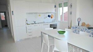 Una cucina moderna con mobili bianchi, un tavolo da pranzo con sedie bianche e una finestra con vista su un edificio con tetto rosso.