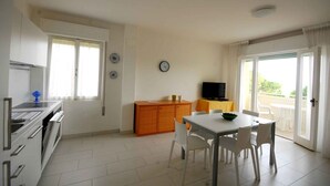 Una cucina moderna con mobili bianchi, un'area pranzo con tavolo e sedie bianche, e un balcone con vista.