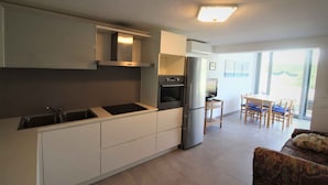 A modern kitchen with built-in appliances, a dining area with a table and chairs, and a large window providing natural light. - Holiday apartment with common garden (Lignano Sabbiadoro)