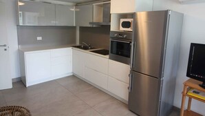 A modern kitchen with white cabinets, stainless steel appliances, and a built-in microwave. - Holiday apartment with common garden (Lignano Sabbiadoro)