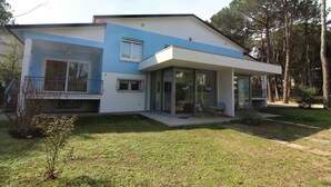Una casa moderna de dos pisos con fachada azul y blanca, un porche cubierto con mobiliario, y un césped cuidado.