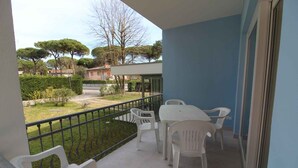 Un balcón con sillas de plástico blanco y una mesa, con vistas a un jardín con árboles y un sendero.