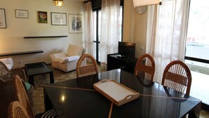A hotel room with a dining table, chairs, a sofa, a TV, and framed pictures on the wall. - Holiday apartment mit Pool (Lignano Sabbiadoro)