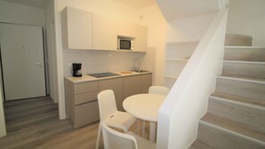 A compact kitchen with a microwave, sink, and white chairs around a small table. - Holiday apartment mit Balkon (Lignano Sabbiadoro)