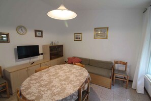 A cozy living room with a round table, a sofa, a TV, and a cabinet. - Holiday apartment mit Terrasse (Lignano Sabbiadoro)