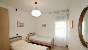 Una stanza piccola e pulita con due letti singoli, uno specchio rotondo e una luce a soffitto.