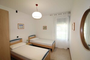 Une petite chambre propre, avec deux lits simples, un miroir rond et un luminaire au plafond.