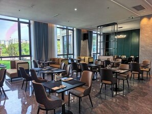 Un espace de restauration moderne, doté de plusieurs tables et chaises, de grandes fenêtres et offrant une vue sur l’extérieur.