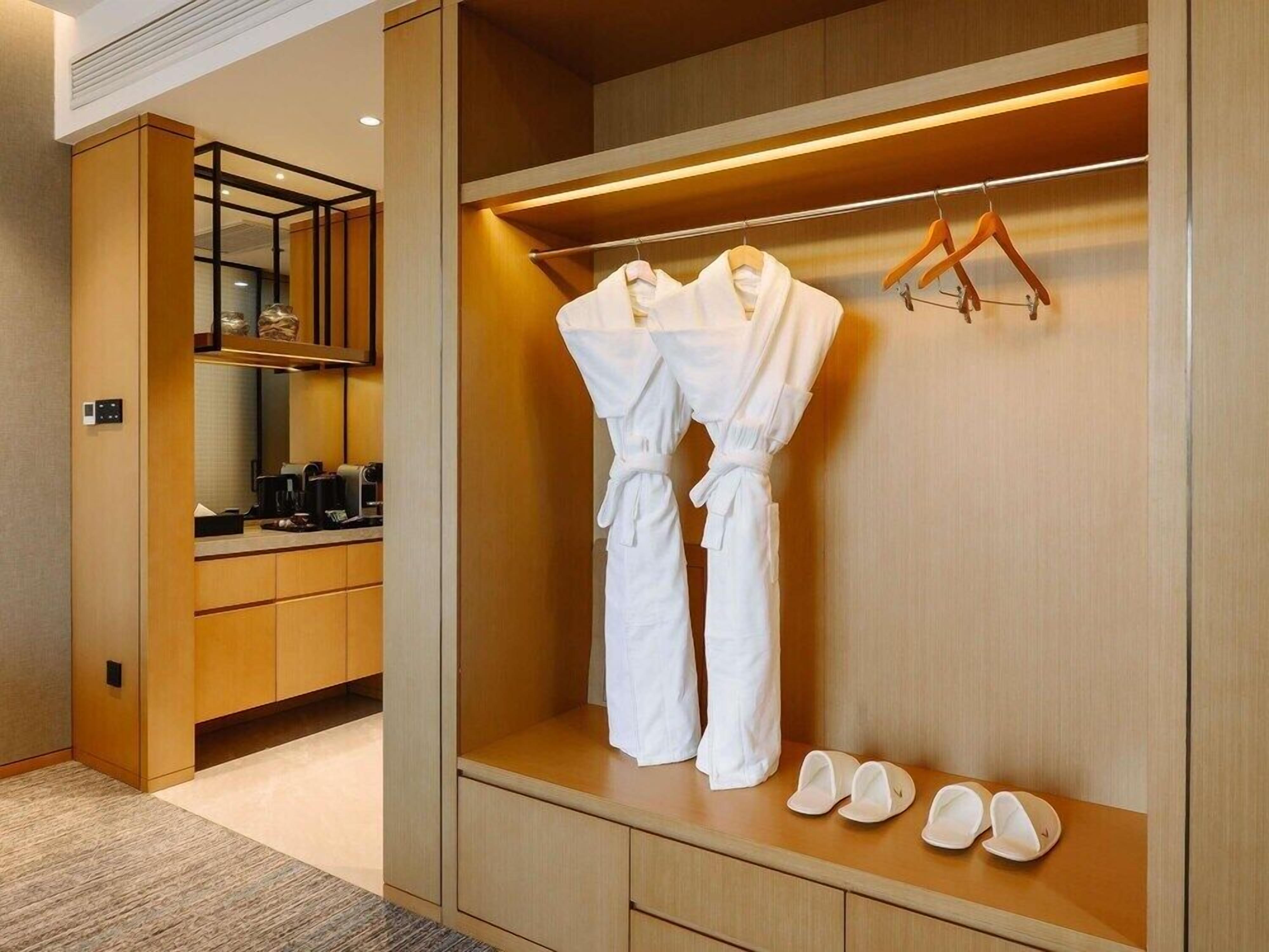 A hotel room with a walk-in closet containing a robe and slippers.