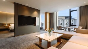 Une chambre d’hôtel moderne dotée d’une télévision à écran plat, d’un canapé, d’une table basse et offrant une vue sur un immeuble grâce à de grandes fenêtres.
