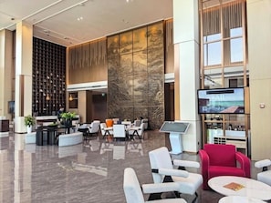 A modern lobby with a reception desk, seating area, and a large screen displaying the word 'EXIT'. - Movenpick Tashkent Old City (Tashkent)