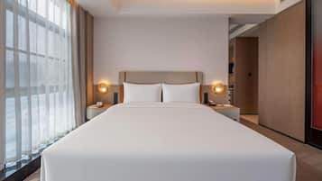 A hotel room with a large bed, two bedside tables with lamps, a view through sheer curtains, and a modern design.
