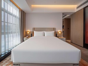 Una habitació d'hotel amb un llit gran, dues taules de nit amb làmpades, vista a través de cortines transparents i un disseny modern.
