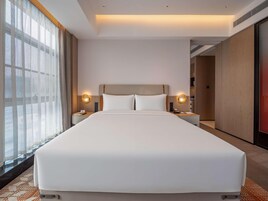 Habitación de hotel con una cama grande, dos mesitas de noche con lámparas, vistas a través de cortinas translúcidas y un diseño moderno.