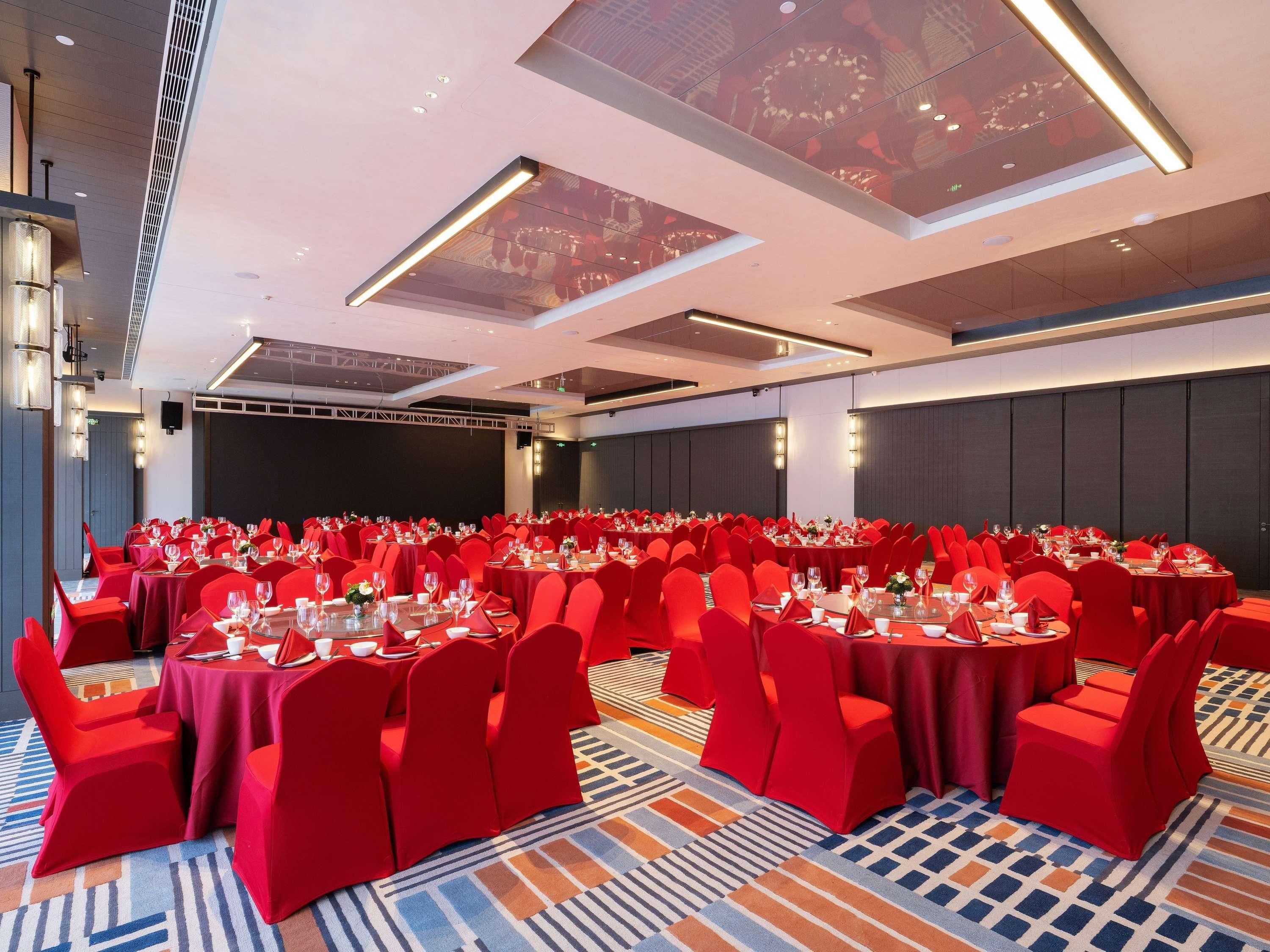 A large conference room with round tables, red chairs, and a patterned carpet.