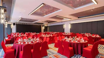 A large conference room with round tables, red chairs, and a patterned carpet.