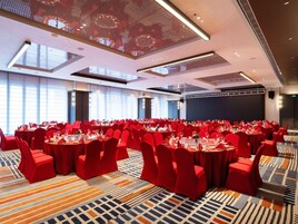 Un salón de conferencias amplio con mesas redondas, sillas rojas y una alfombra estampada.