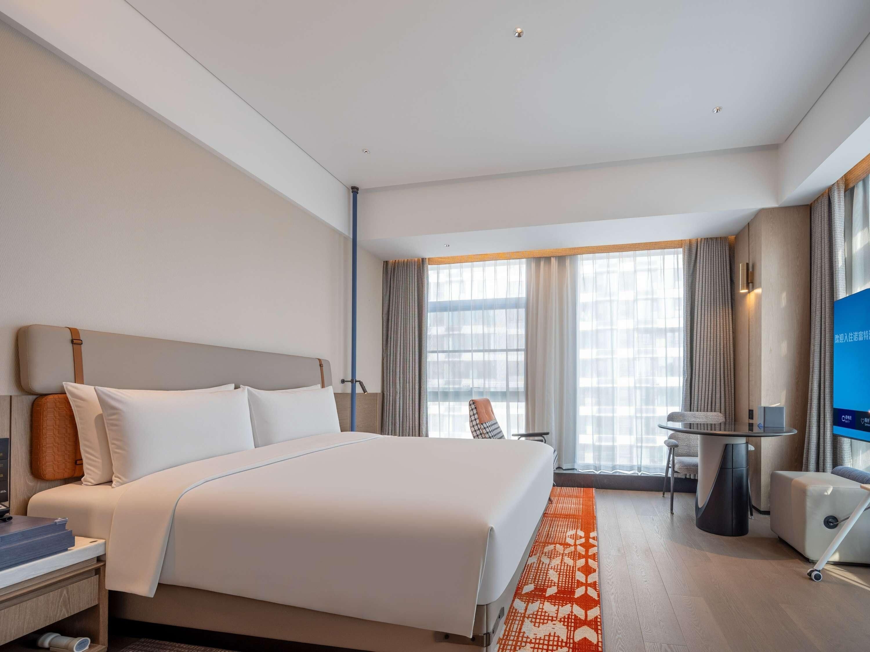 Een hotelkamer met een bed, nachtkastje, stoel, televisie en een raam met gordijnen.