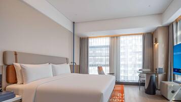 A hotel room with a bed, bedside table, chair, TV, and a window with curtains.