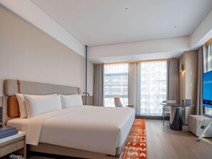 A hotel room with a bed, bedside table, chair, TV, and a window with curtains.
