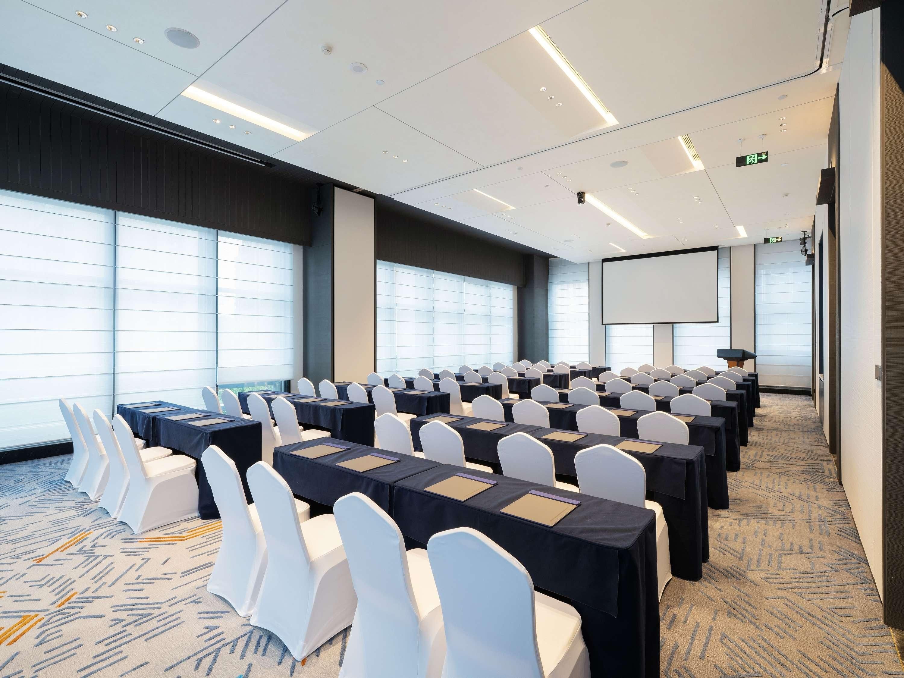 A conference room with rows of tables and chairs, a projector screen, and large windows.
