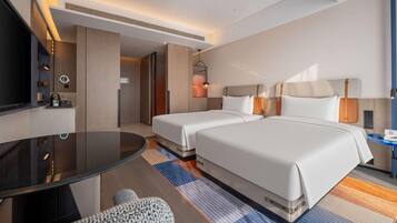 A hotel room with two beds, a TV, a desk, and a small seating area.