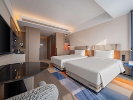 A hotel room with two beds, a TV, a desk, and a small seating area.