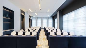 A conference room with rows of tables and chairs, large windows, and a patterned carpet.
