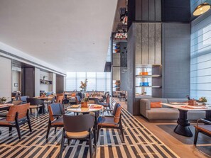 A modern hotel lobby with a high ceiling, large windows, and a mix of seating areas including tables and sofas. - Novotel Zibo New Hongcheng (Zibo)
