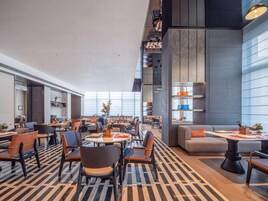 Un moderno vestíbulo de hotel con techo alto, ventanas amplias y una variedad de zonas de estar, incluidas mesas y sofás.