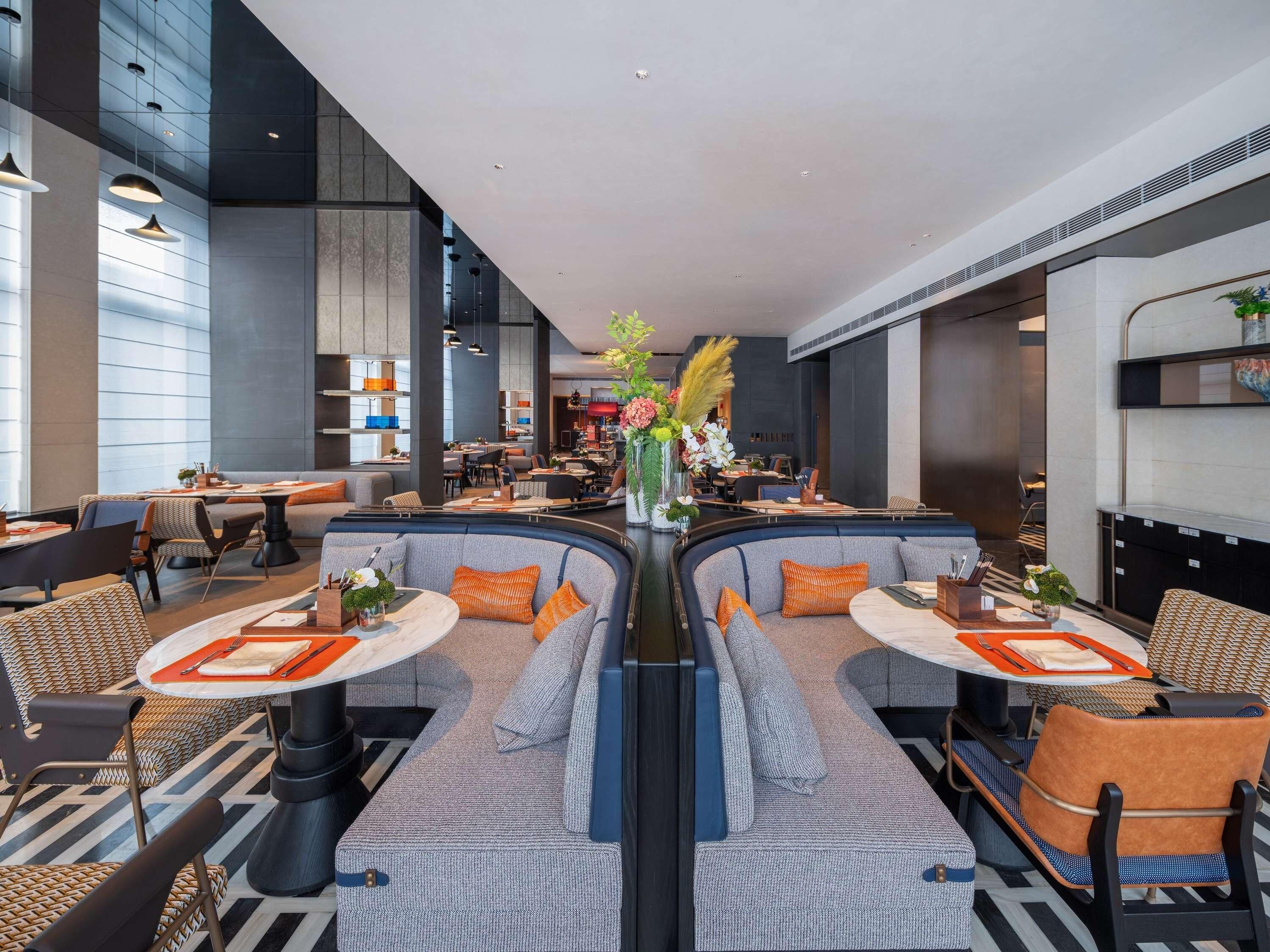 A modern hotel lobby with a central seating area, tables, and a bar.