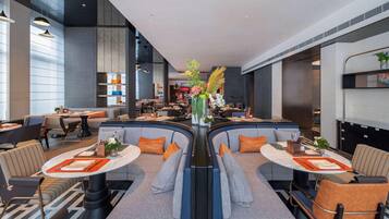 A modern hotel lobby with a central seating area, tables, and a bar.