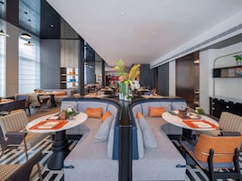 A modern hotel lobby with a central seating area, tables, and a bar.